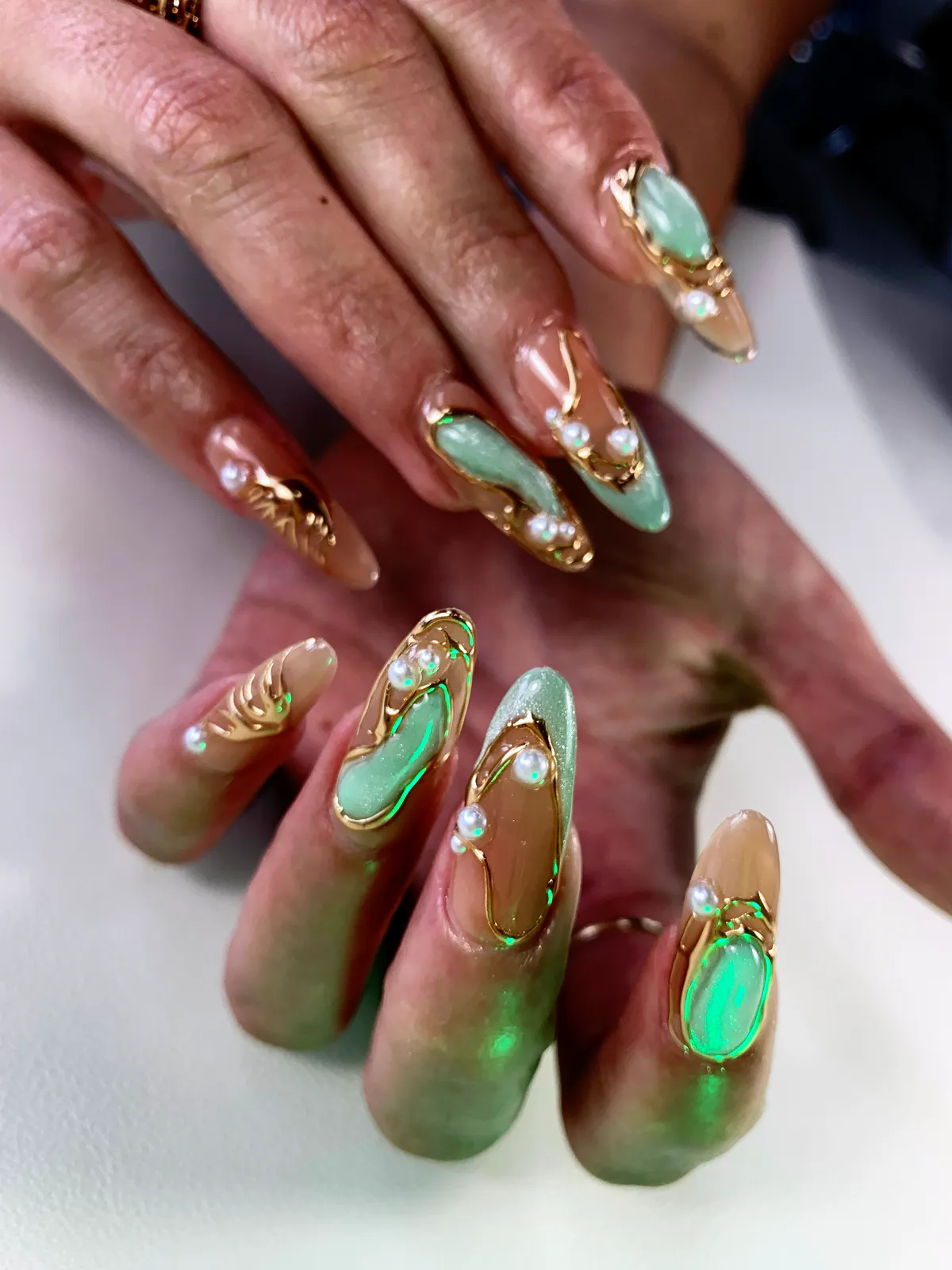 Long nude almond nails with gold swirls, mint inlays and pearls, by BeautyFusionClau in Sarasota, Florida